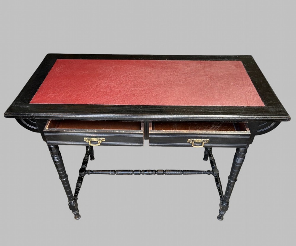 A late Victorian ebonised writing desk featuring a red leather top insert, two drawers with brass handles, turned legs, and an H-stretcher. View III