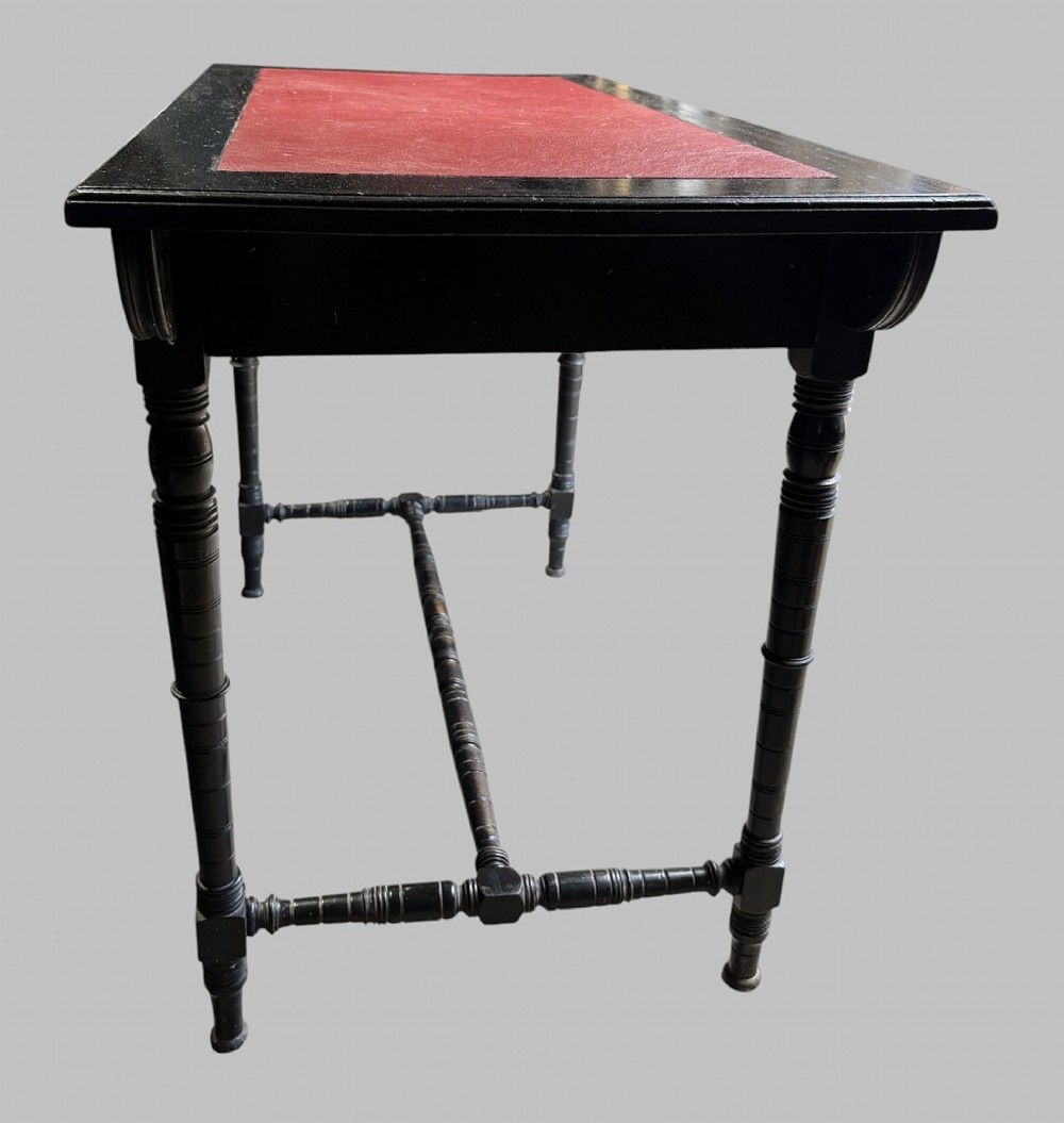 A late Victorian ebonised writing desk featuring a red leather top insert, two drawers with brass handles, turned legs, and an H-stretcher. View IV