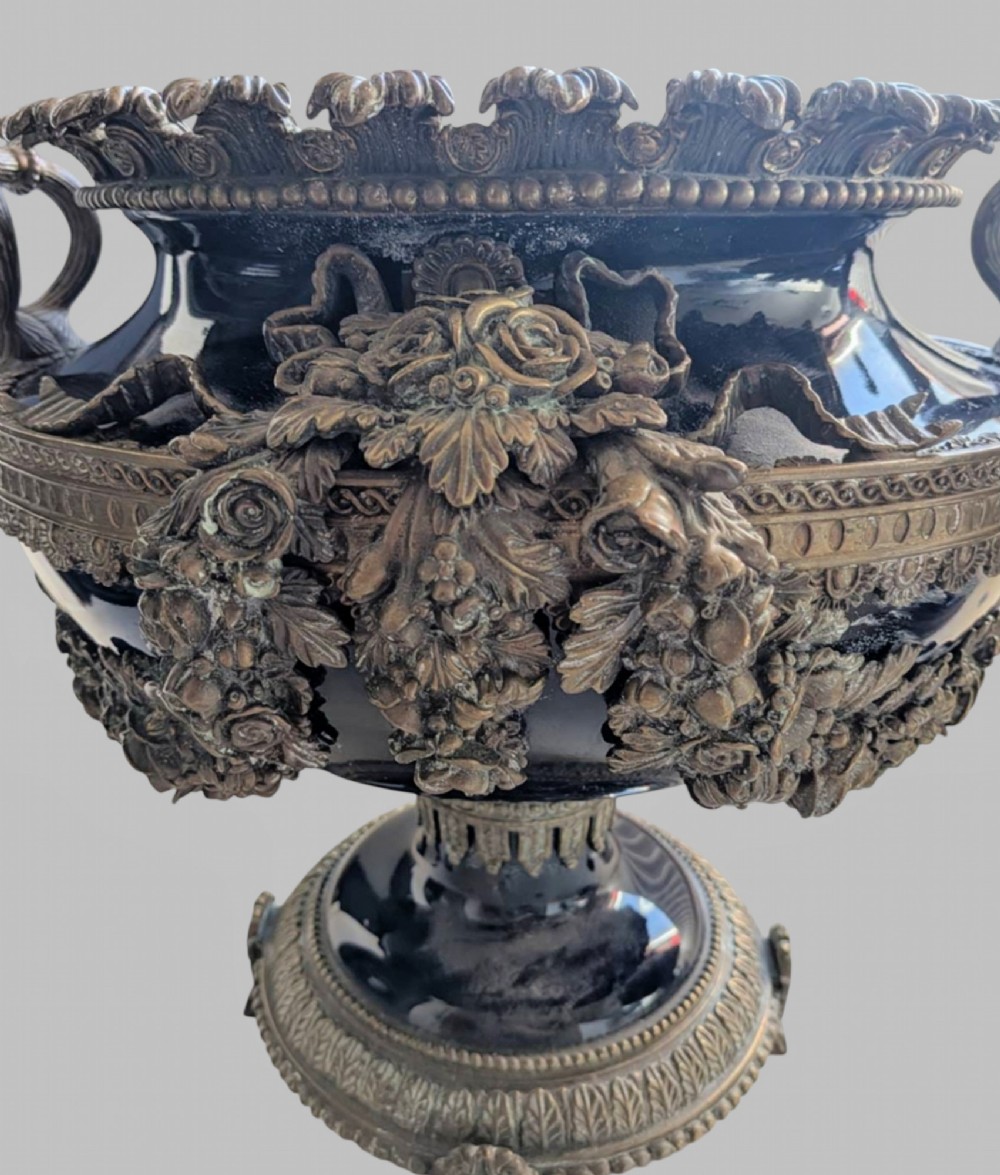 A pair of deep cobalt blue glazed ceramic urn-shaped jardinieres adorned with ornate gilt bronze mounts, floral swags, and decorative handles, set on footed bases. View V