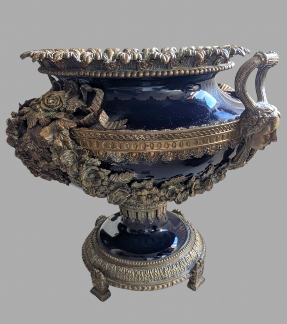 A pair of deep cobalt blue glazed ceramic urn-shaped jardinieres adorned with ornate gilt bronze mounts, floral swags, and decorative handles, set on footed bases. View VI