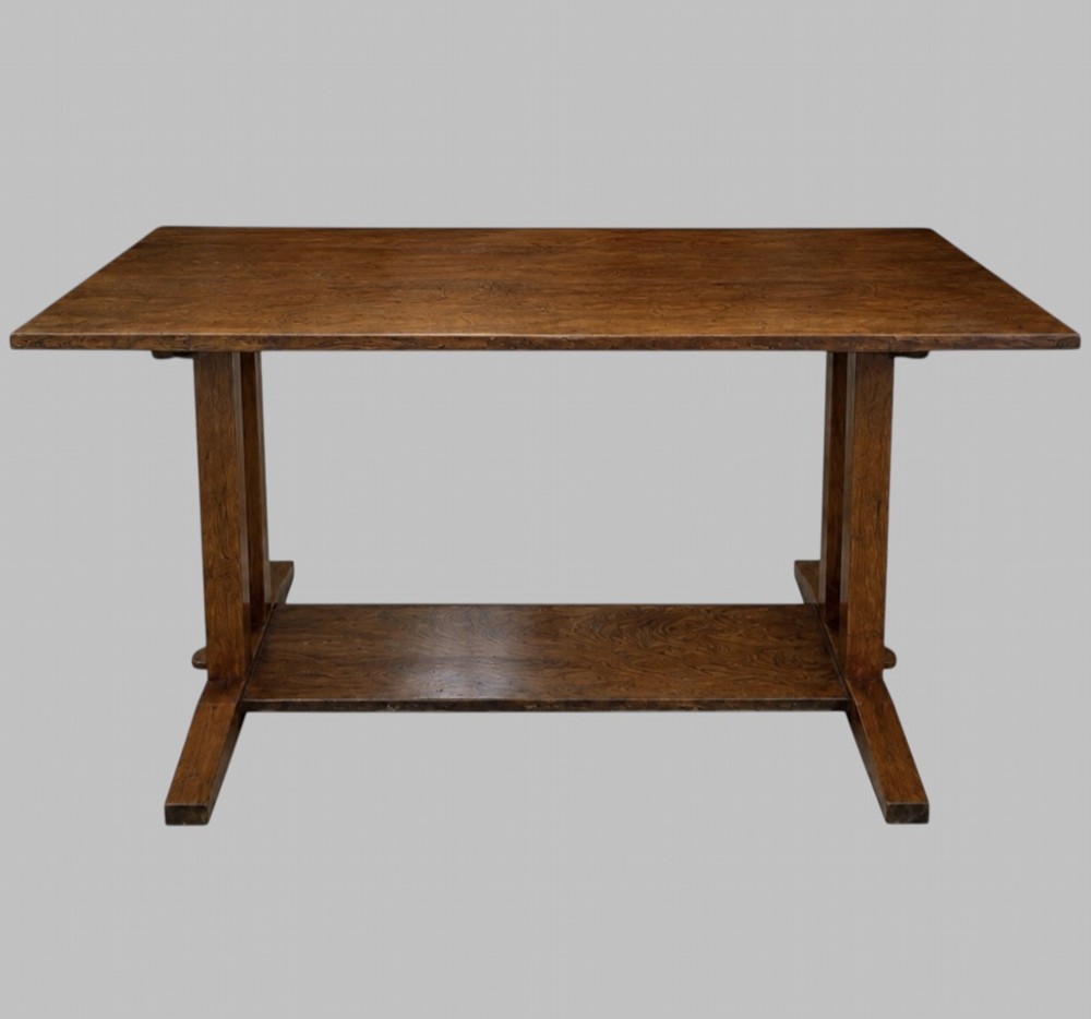 An Arts and Crafts solid oak dining table featuring a rectangular top, twin upright trestle end supports, and a low solid wooden stretcher shelf. View II