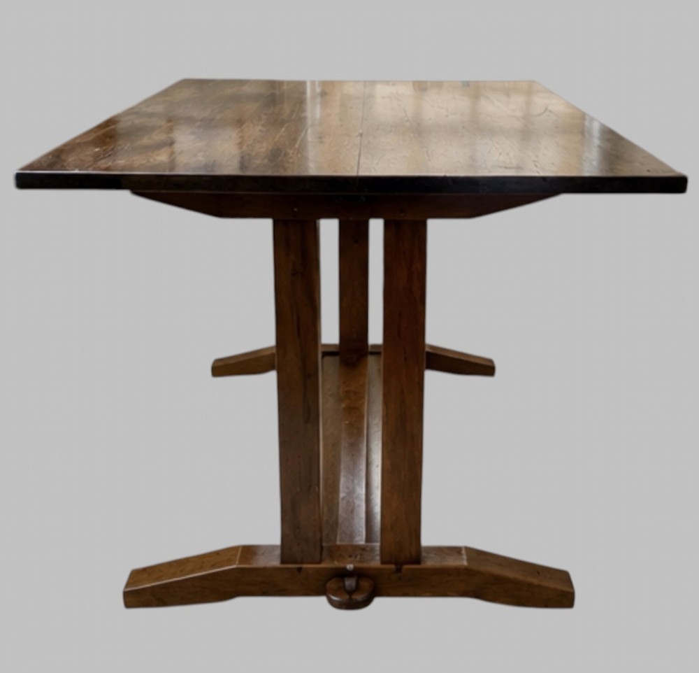 An Arts and Crafts solid oak dining table featuring a rectangular top, twin upright trestle end supports, and a low solid wooden stretcher shelf. View III