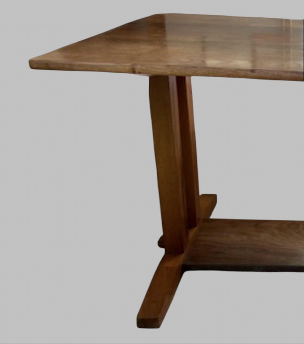 An Arts and Crafts solid oak dining table featuring a rectangular top, twin upright trestle end supports, and a low solid wooden stretcher shelf. View IV