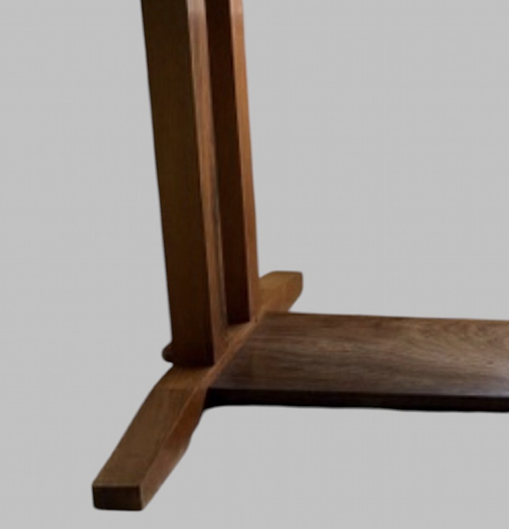 An Arts and Crafts solid oak dining table featuring a rectangular top, twin upright trestle end supports, and a low solid wooden stretcher shelf. View V