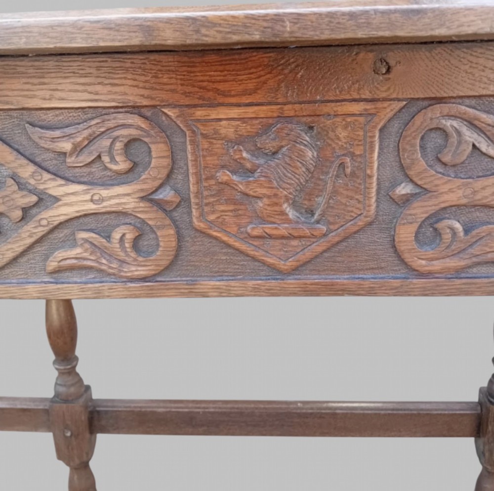 A dark oak hall table featuring turned legs, lower perimeter stretchers, a carved scrollwork frieze, and a carved central medallion on the top surface. View V