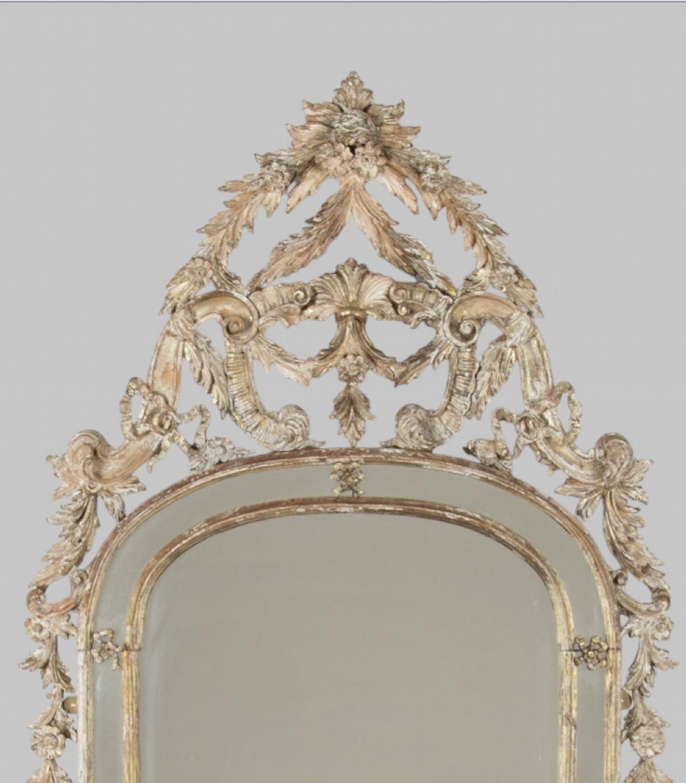 An antique nineteenth-century French giltwood mirror featuring elaborate carved cresting with foliage motifs and an arched frame. View II