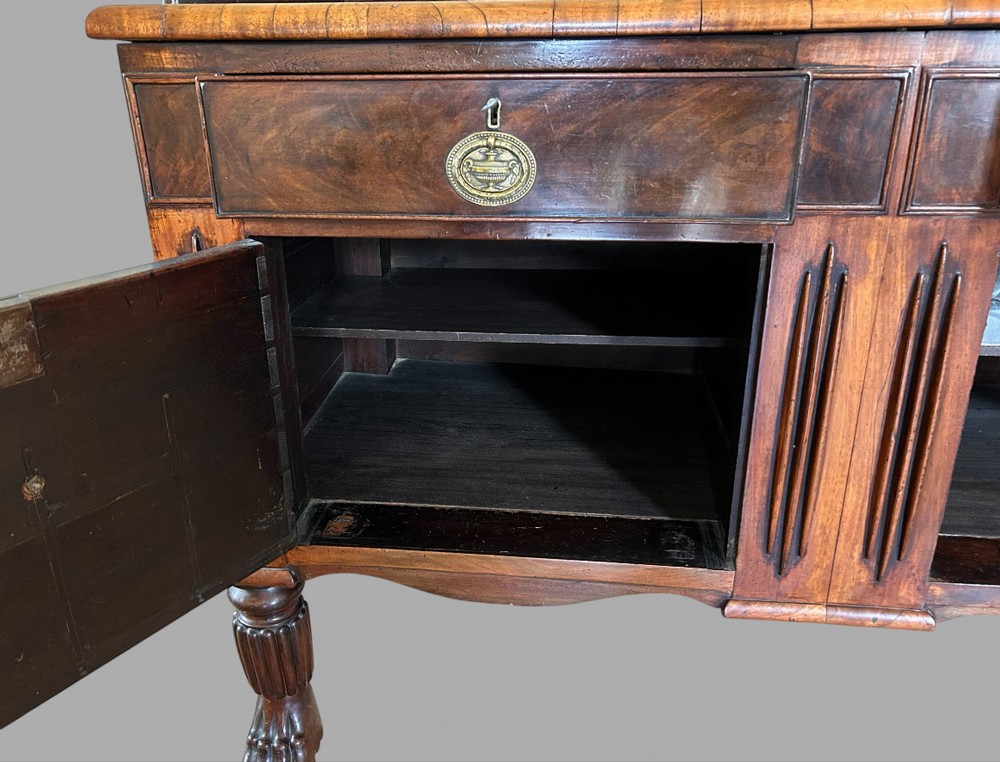 A 19th-century flame mahogany sideboard featuring two upper drawers, two cabinet doors, reeded pilasters, oval brass handles, a low gallery back, and carved paw feet. View V