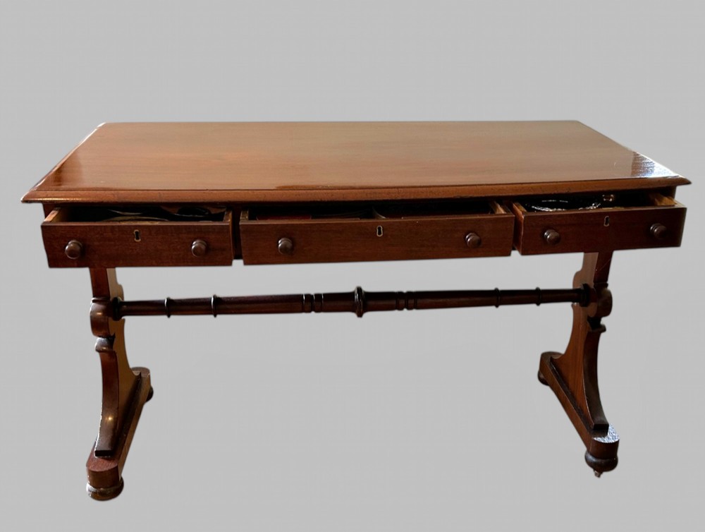 A rectangular mahogany library table featuring three frieze drawers with round timber handles and a lower turned stretcher resting on shaped trestle feet. View VI