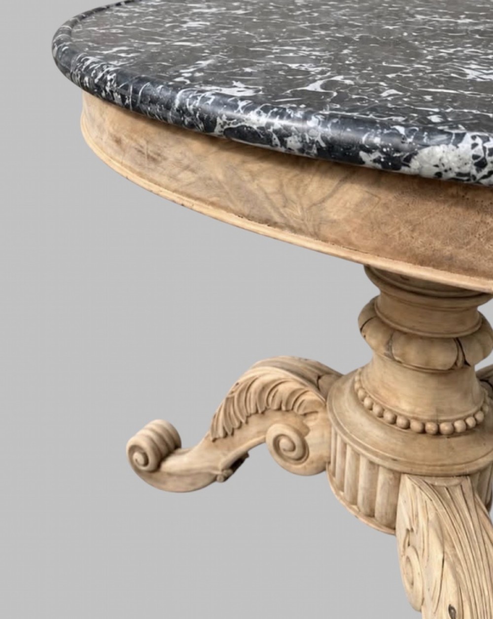 A circular antique French gueridon table featuring a dark grey mottled marble top supported by a carved bleached walnut pedestal and tripod scrolled legs. View IV