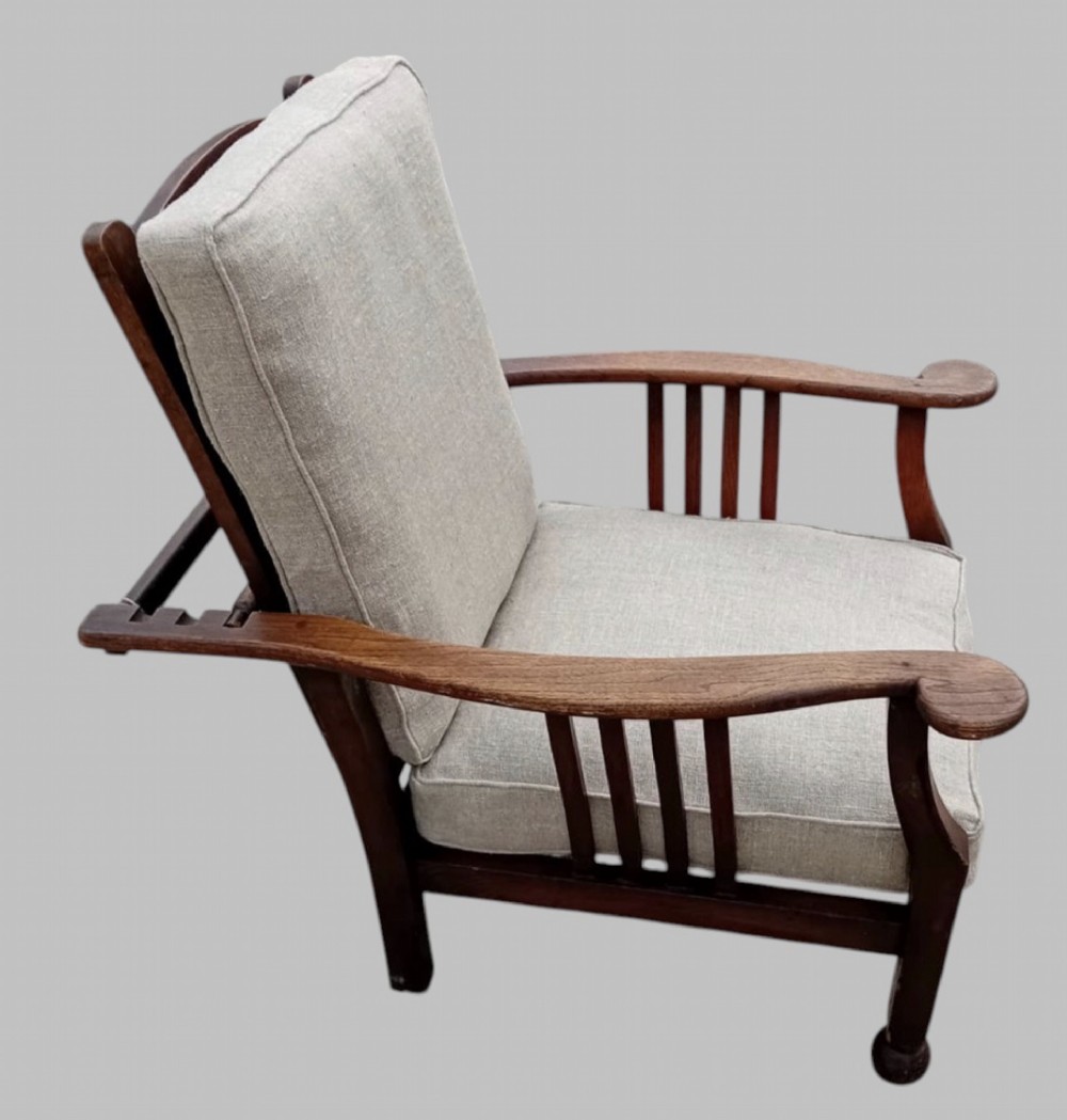 An Arts and Crafts dark oak reclining armchair with wide curved armrests and light grey fabric back and seat cushions. View II