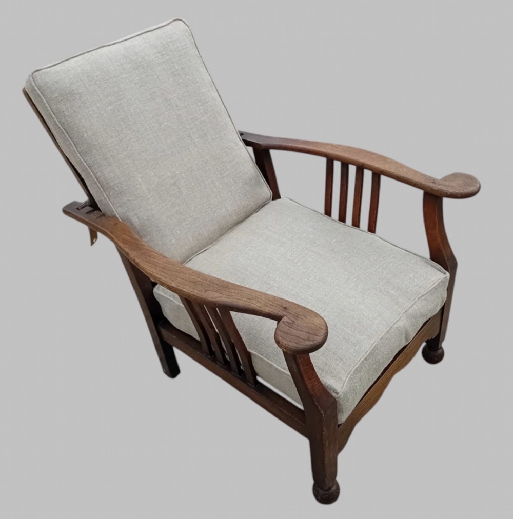 An Arts and Crafts dark oak reclining armchair with wide curved armrests and light grey fabric back and seat cushions. View III