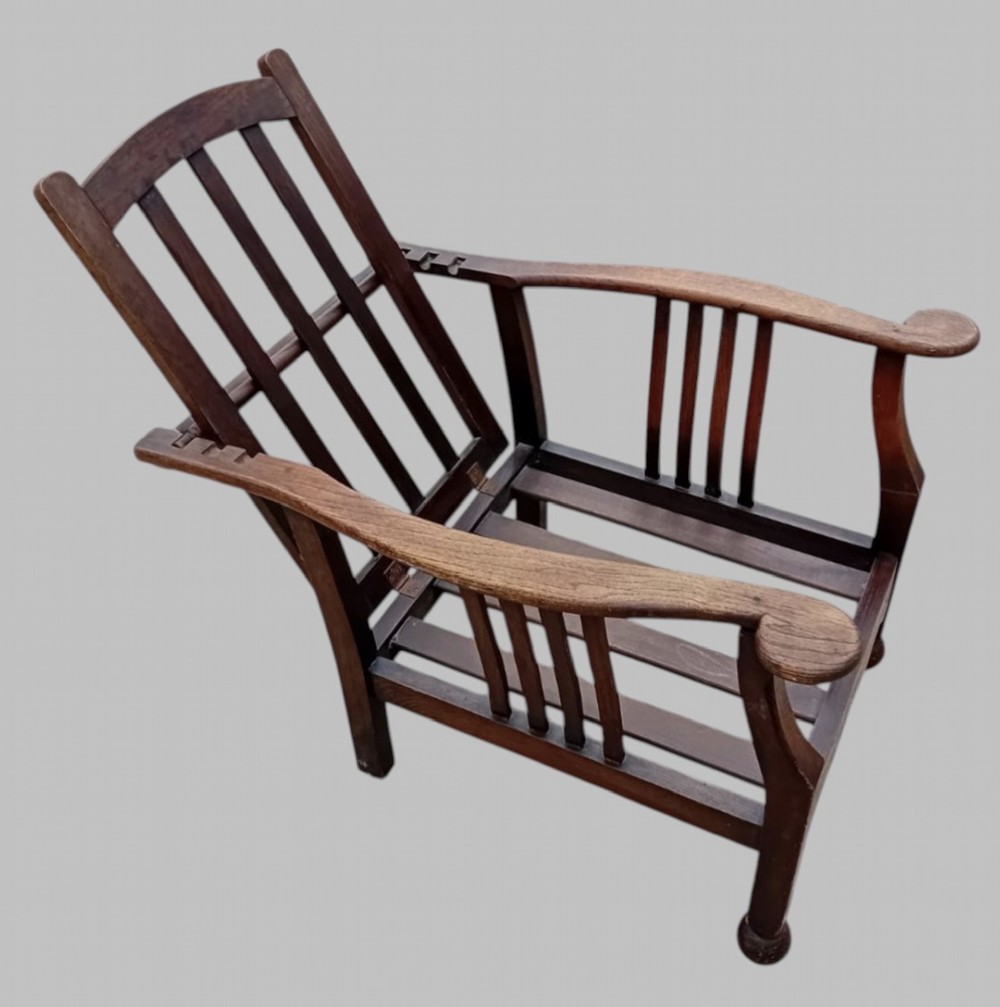 An Arts and Crafts dark oak reclining armchair with wide curved armrests and light grey fabric back and seat cushions. View IV