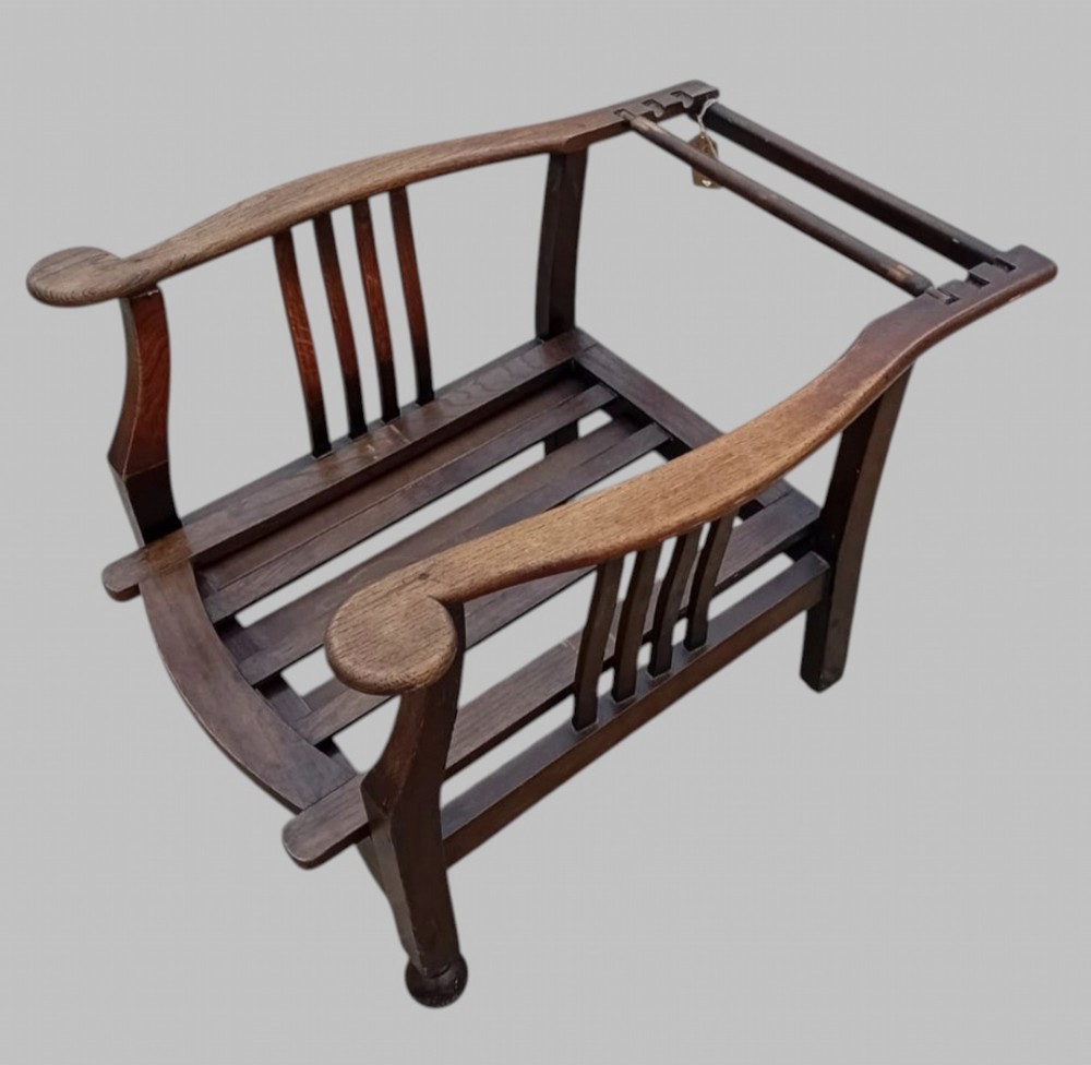 An Arts and Crafts dark oak reclining armchair with wide curved armrests and light grey fabric back and seat cushions. View V