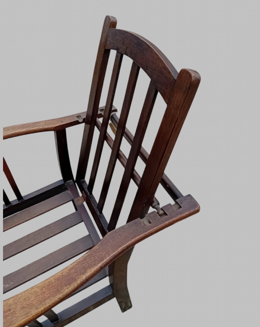 An Arts and Crafts dark oak reclining armchair with wide curved armrests and light grey fabric back and seat cushions. View VI