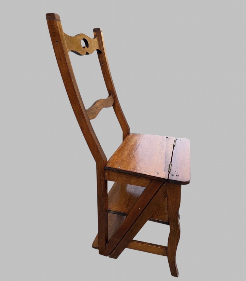 An Arts and Crafts style warm brown oak metamorphic library chair featuring a pierced heart-shaped cutout on the top rail and a hinged seat mechanism. View IV