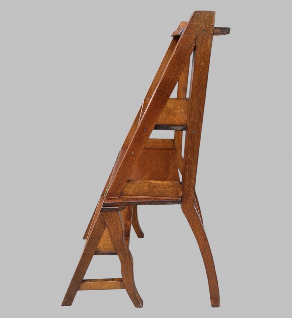 An Arts and Crafts style warm brown oak metamorphic library chair featuring a pierced heart-shaped cutout on the top rail and a hinged seat mechanism. View V