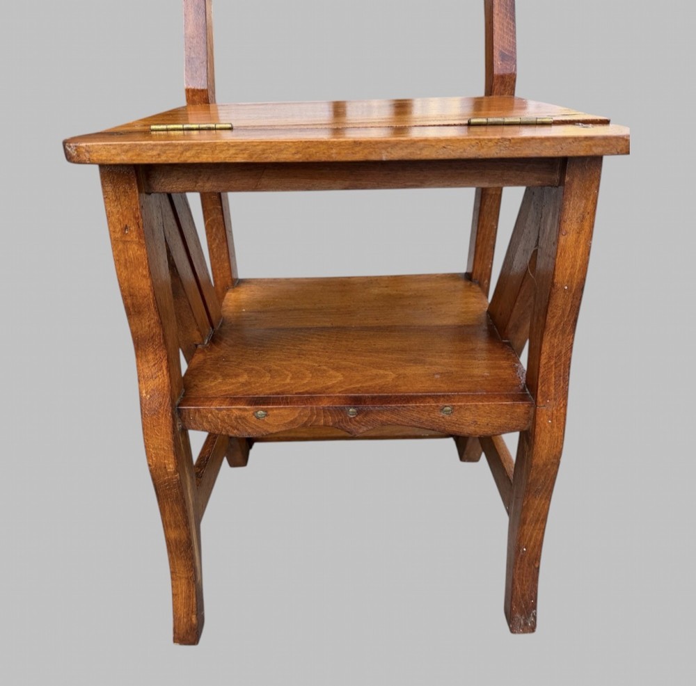 An Arts and Crafts style warm brown oak metamorphic library chair featuring a pierced heart-shaped cutout on the top rail and a hinged seat mechanism. View VI