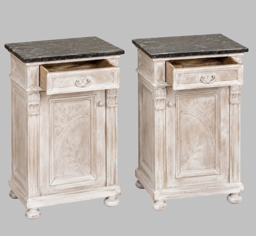 A matching pair of mid-nineteenth-century off-white painted wooden bedside cabinets featuring dark marble tops, single drawers, fluted side pilasters, carved floral door panels, and turned bun feet. View II