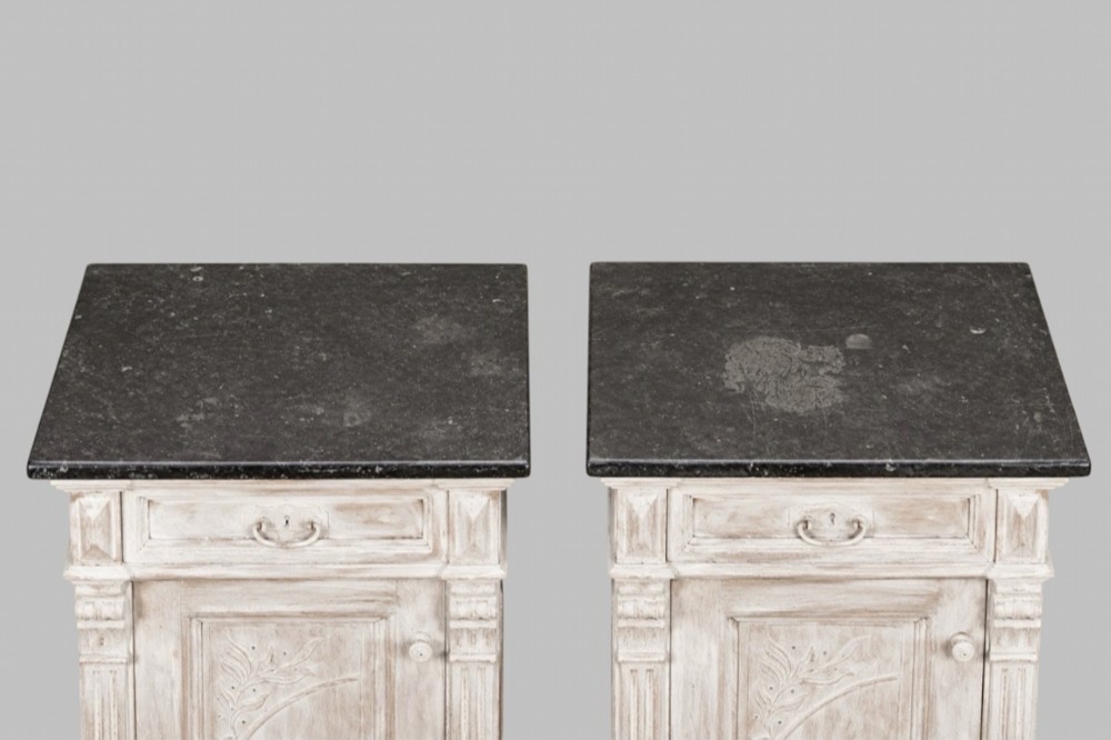 A matching pair of mid-nineteenth-century off-white painted wooden bedside cabinets featuring dark marble tops, single drawers, fluted side pilasters, carved floral door panels, and turned bun feet. View IV
