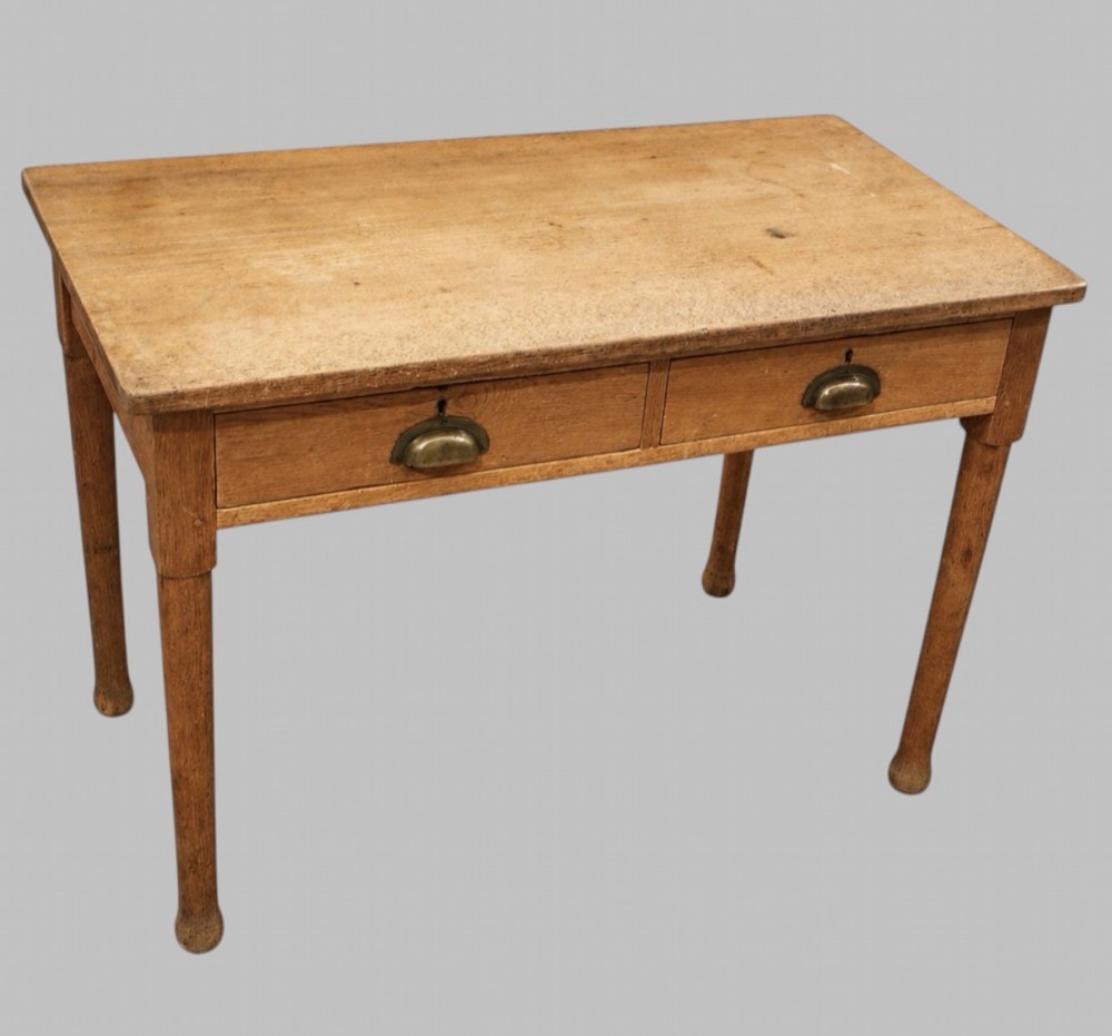 An early 20th-century light oak work table featuring a rectangular top, two frieze drawers with brass cup handles, and turned legs.