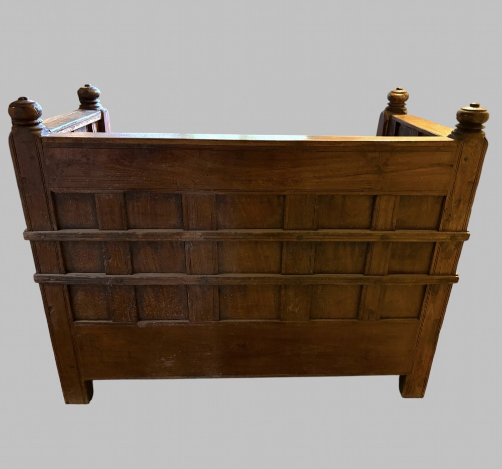 A carved dark hardwood storage bench with a hinged lid seat, geometric panelled backrest, corner post finials, and iron fittings. View IV