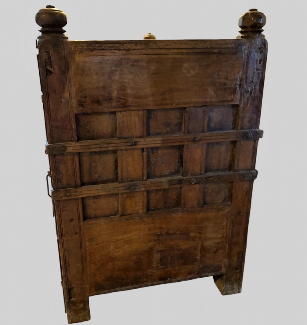 A carved dark hardwood storage bench with a hinged lid seat, geometric panelled backrest, corner post finials, and iron fittings. View V