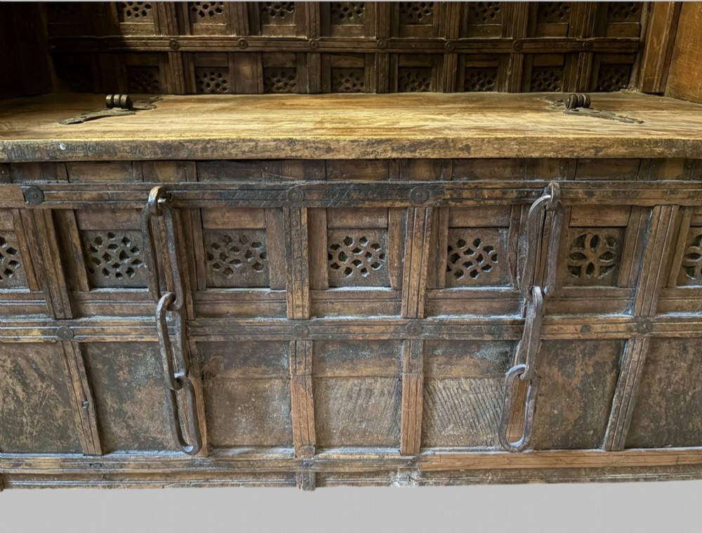 A carved dark hardwood storage bench with a hinged lid seat, geometric panelled backrest, corner post finials, and iron fittings. View VI
