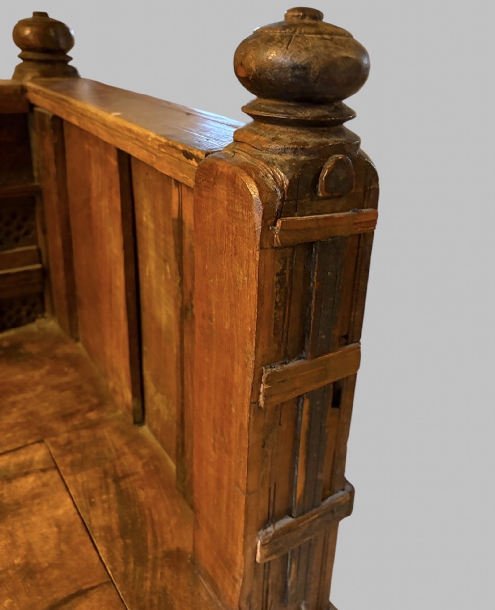 A carved dark hardwood storage bench with a hinged lid seat, geometric panelled backrest, corner post finials, and iron fittings. View VII