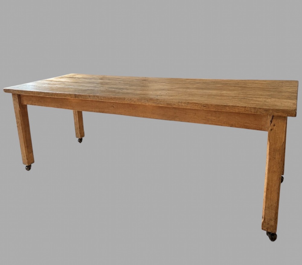 A 19th-century rectangular elm farmhouse table featuring a multi-plank top, straight aprons, four square tapering legs, and small metal castors.