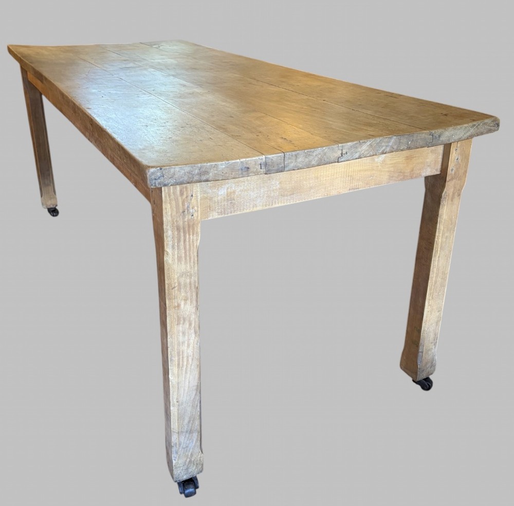 A 19th-century rectangular elm farmhouse table featuring a multi-plank top, straight aprons, four square tapering legs, and small metal castors. View III