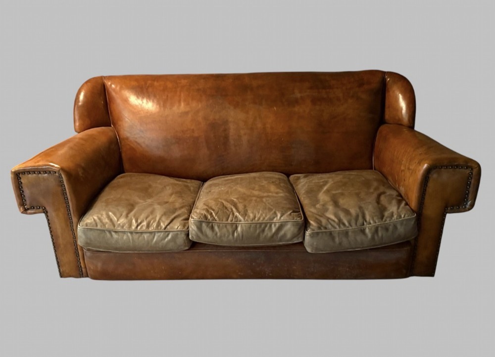 A three-seater Art Deco sofa upholstered in warm brown patinated leather with metal studding along the armrests.