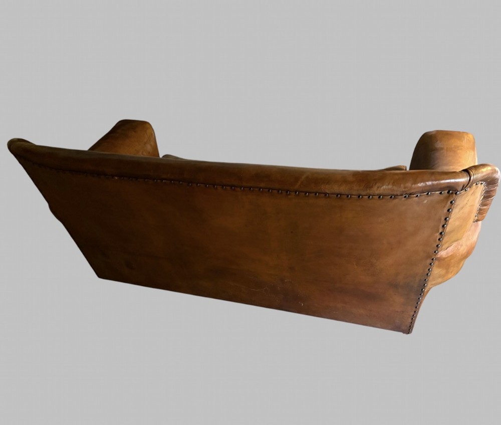 A three-seater Art Deco sofa upholstered in warm brown patinated leather with metal studding along the armrests. View IV