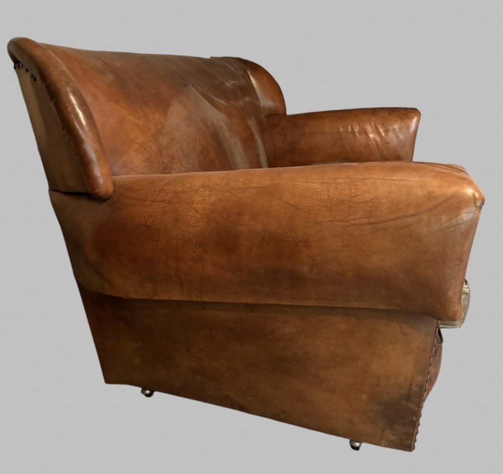 A three-seater Art Deco sofa upholstered in warm brown patinated leather with metal studding along the armrests. View VI