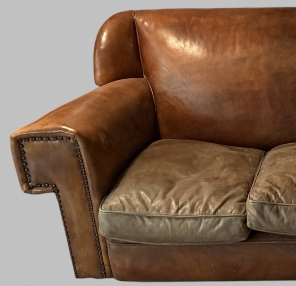 A three-seater Art Deco sofa upholstered in warm brown patinated leather with metal studding along the armrests. View VII