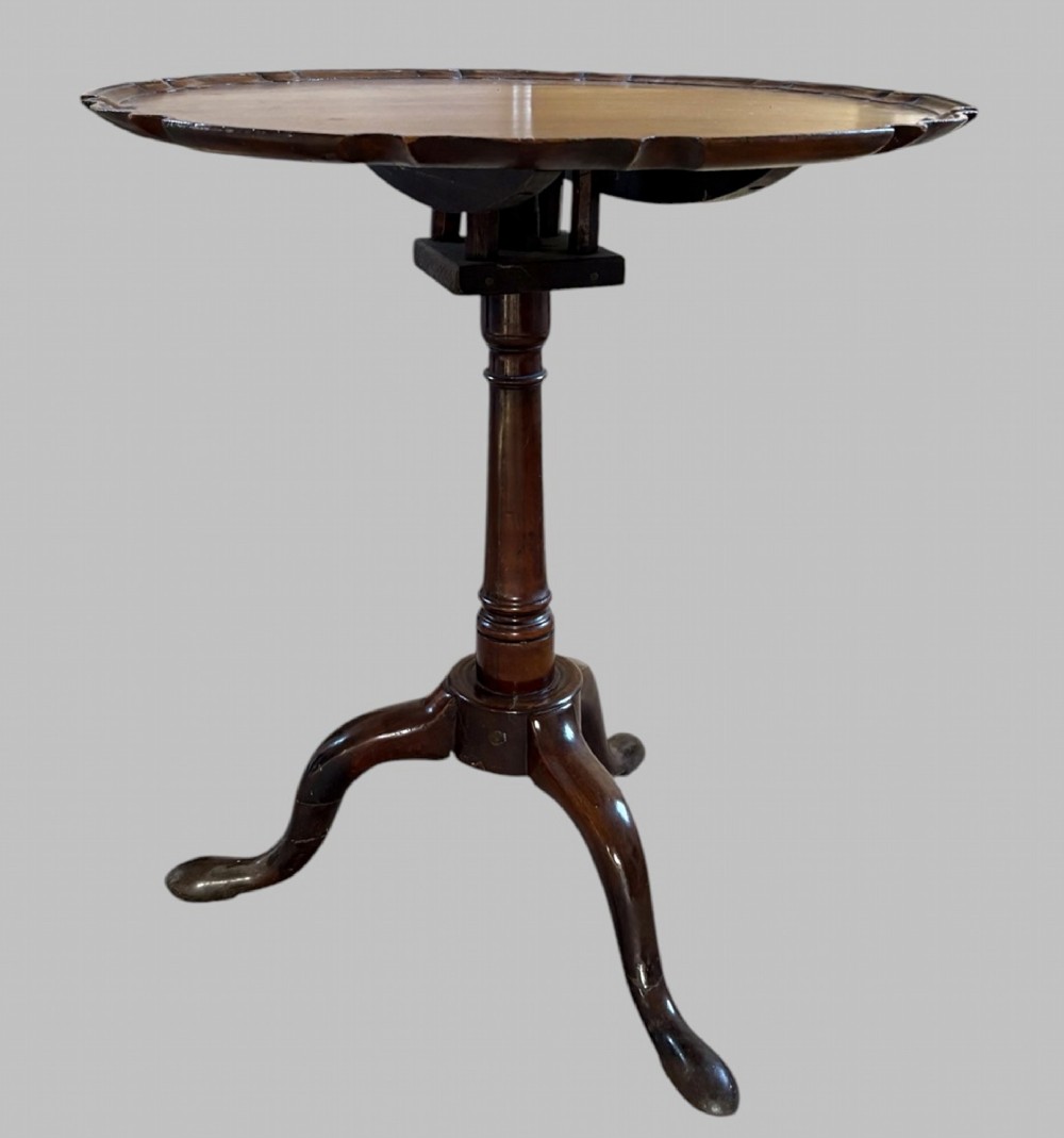 A dark mahogany tripod table featuring a circular pie-crust scalloped top, a turned central column with a birdcage block, and three cabriole legs ending in pad feet.
