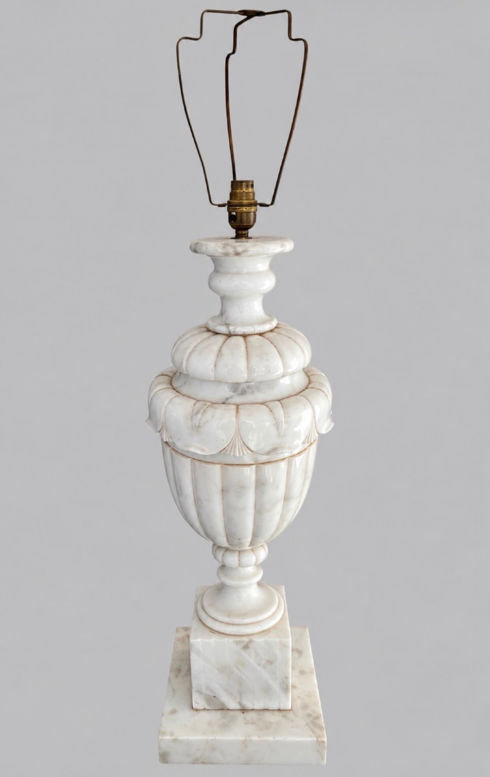 A carved off-white alabaster table lamp base shaped like a classical urn with leaf motifs, resting on a stepped square plinth with a brass harp socket.