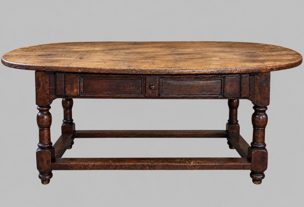 An antique Swedish provincial pine farmhouse table featuring an oval plank top, frieze with drawer moulding, turned baluster legs, and a low rectangular box stretcher.
