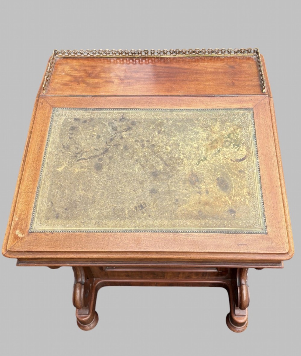 A front view of a Victorian walnut Davenport desk featuring a slanted green leather writing surface, decorative top brass gallery rail, carved front supports, and a panelled wooden body. View IV