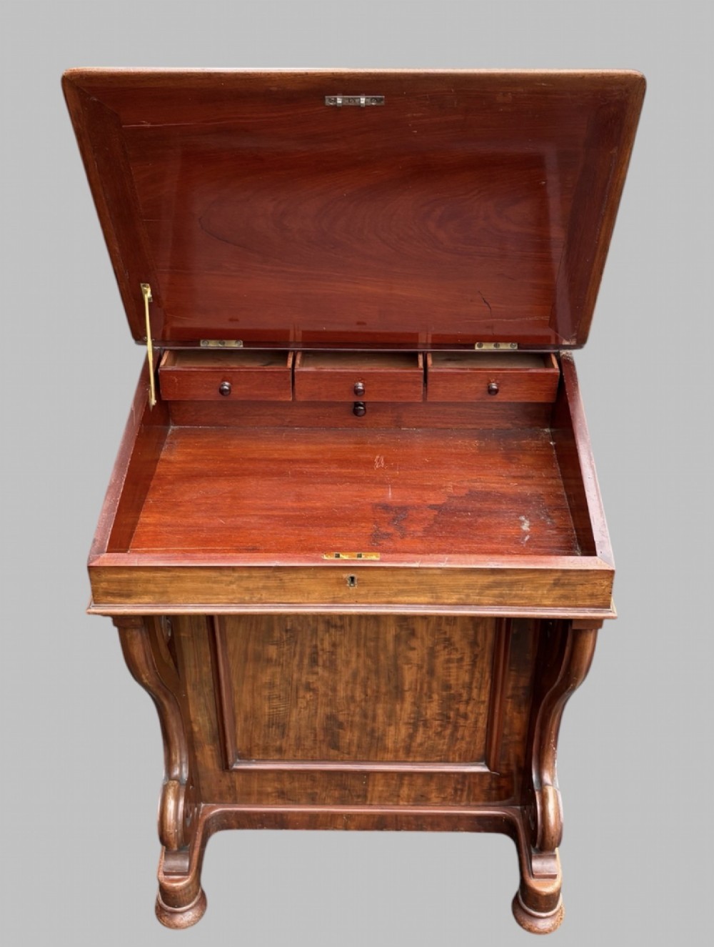 A front view of a Victorian walnut Davenport desk featuring a slanted green leather writing surface, decorative top brass gallery rail, carved front supports, and a panelled wooden body. View V