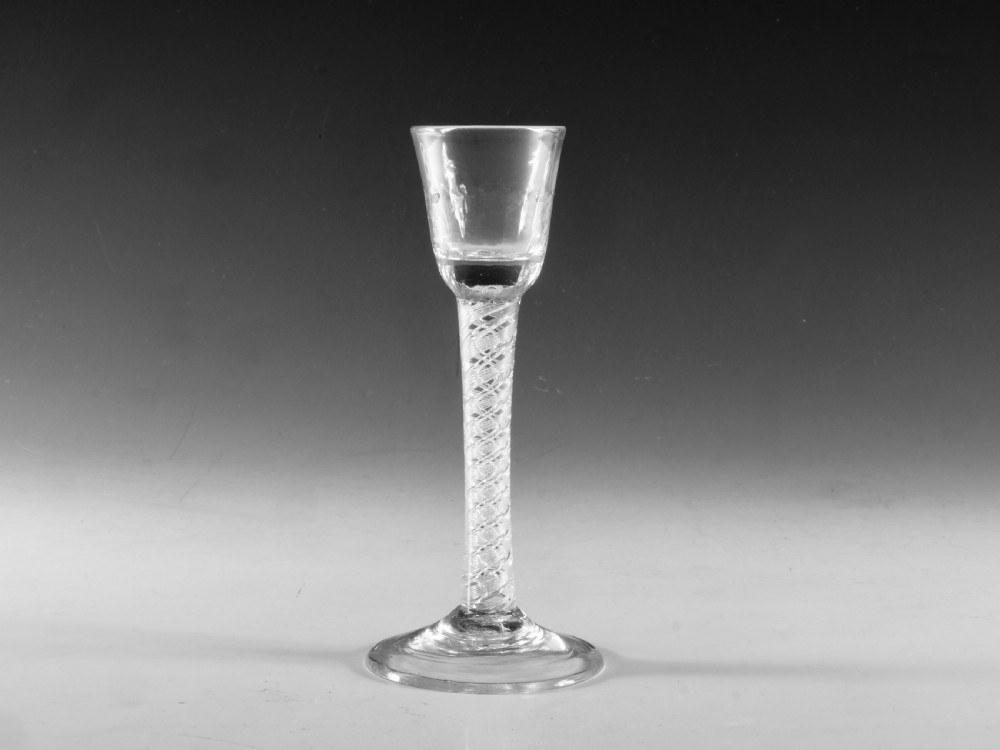 An 18th-century English clear glass cordial featuring a small round funnel bowl, a dense air twist stem, and a flat conical foot.