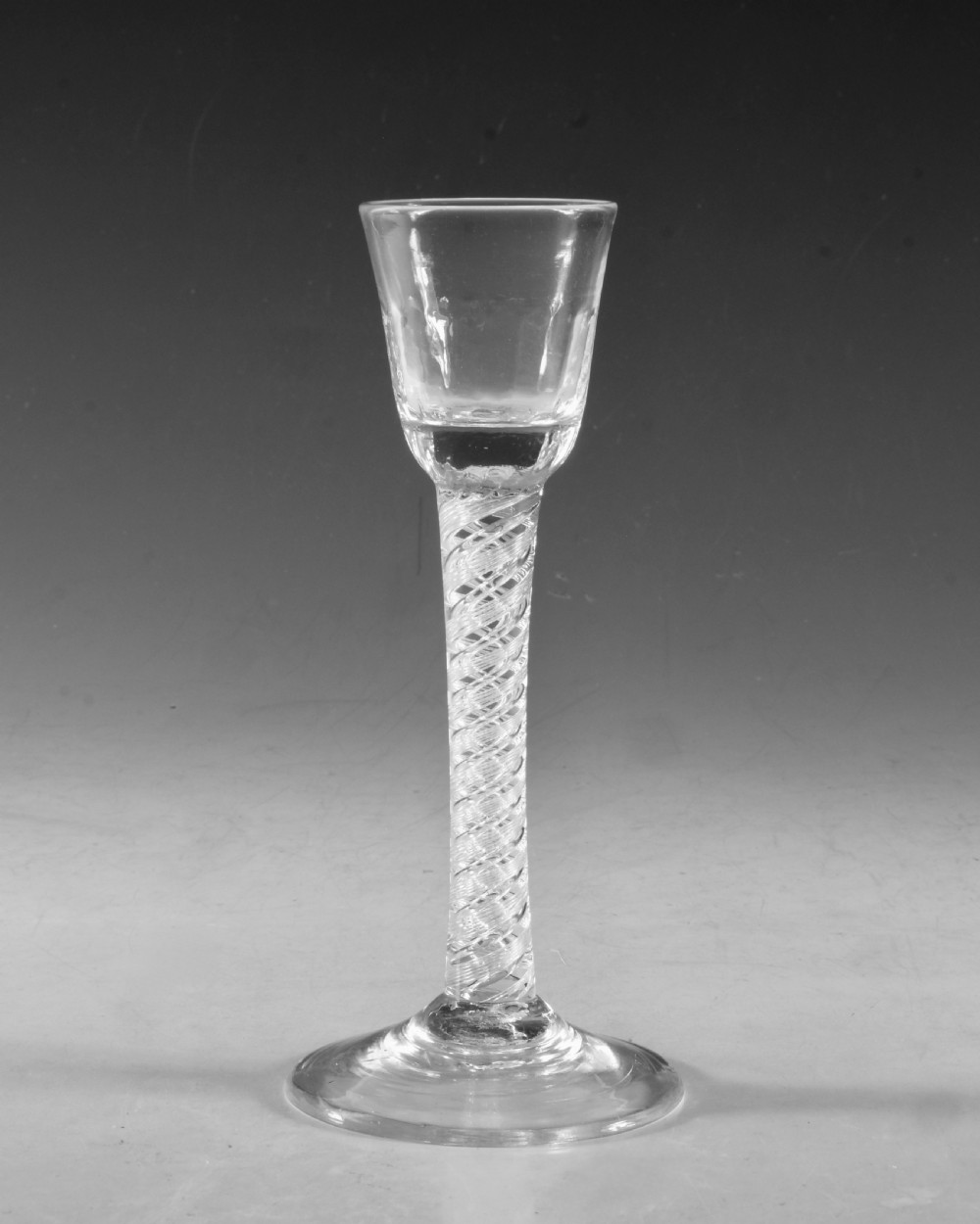 An 18th-century English clear glass cordial featuring a small round funnel bowl, a dense air twist stem, and a flat conical foot. View II