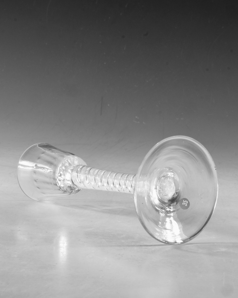 An 18th-century English clear glass cordial featuring a small round funnel bowl, a dense air twist stem, and a flat conical foot. View III