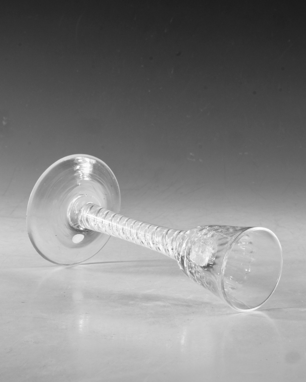An 18th-century English clear glass cordial featuring a small round funnel bowl, a dense air twist stem, and a flat conical foot. View V