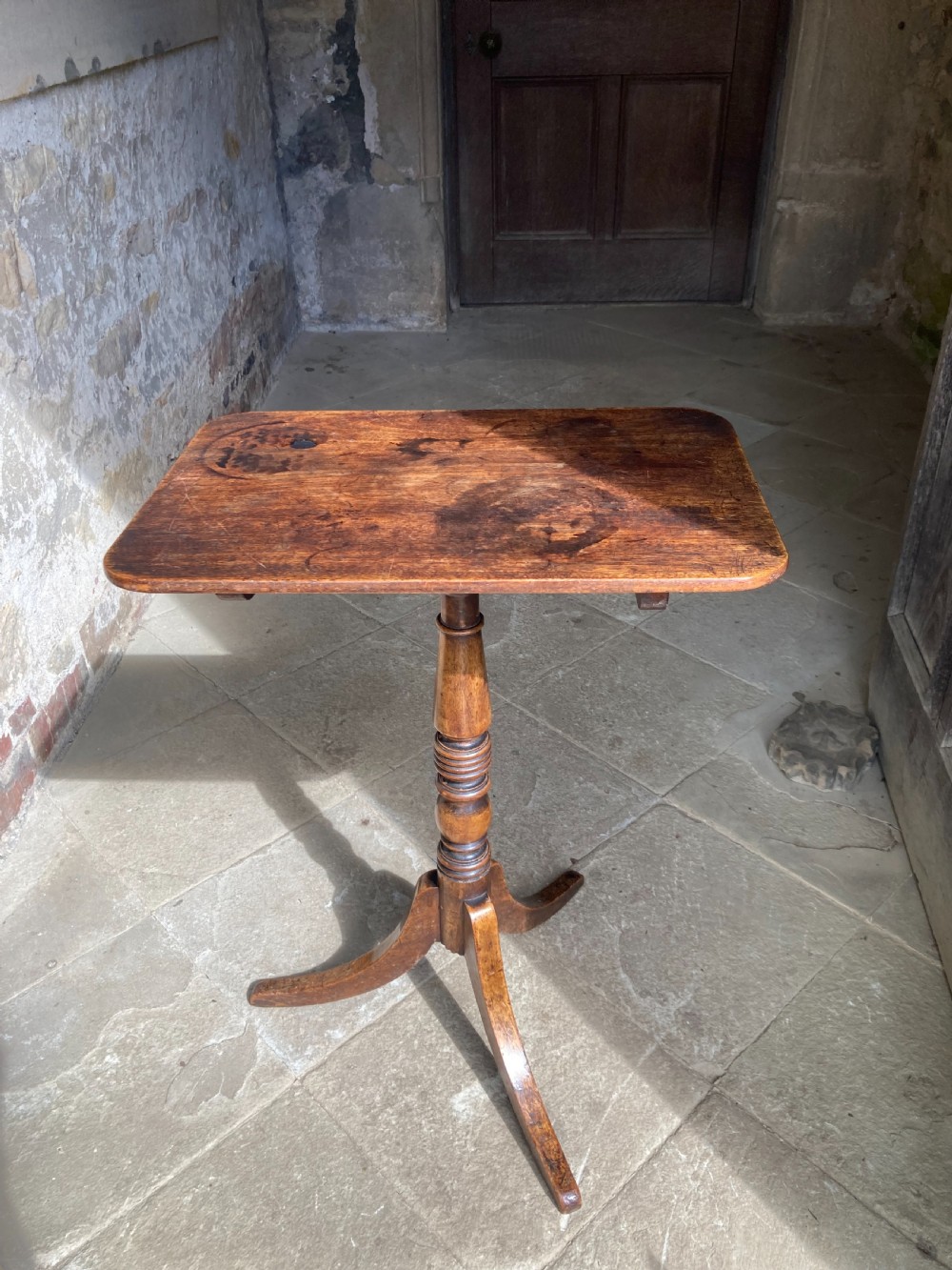 A Regency mahogany tripod table featuring a rectangular surface with rounded corners, a central turned stem, and three splayed legs.