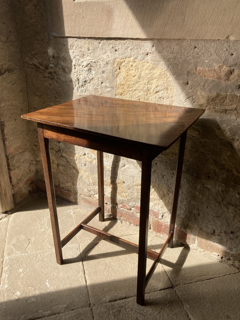 A Regency period mahogany occasional table featuring a rectangular polished top, straight legs, and lower H-stretchers.