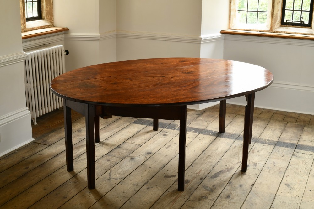 An 18th-century Irish mahogany hunt table featuring an oval drop-leaf top supported by straight wooden legs.