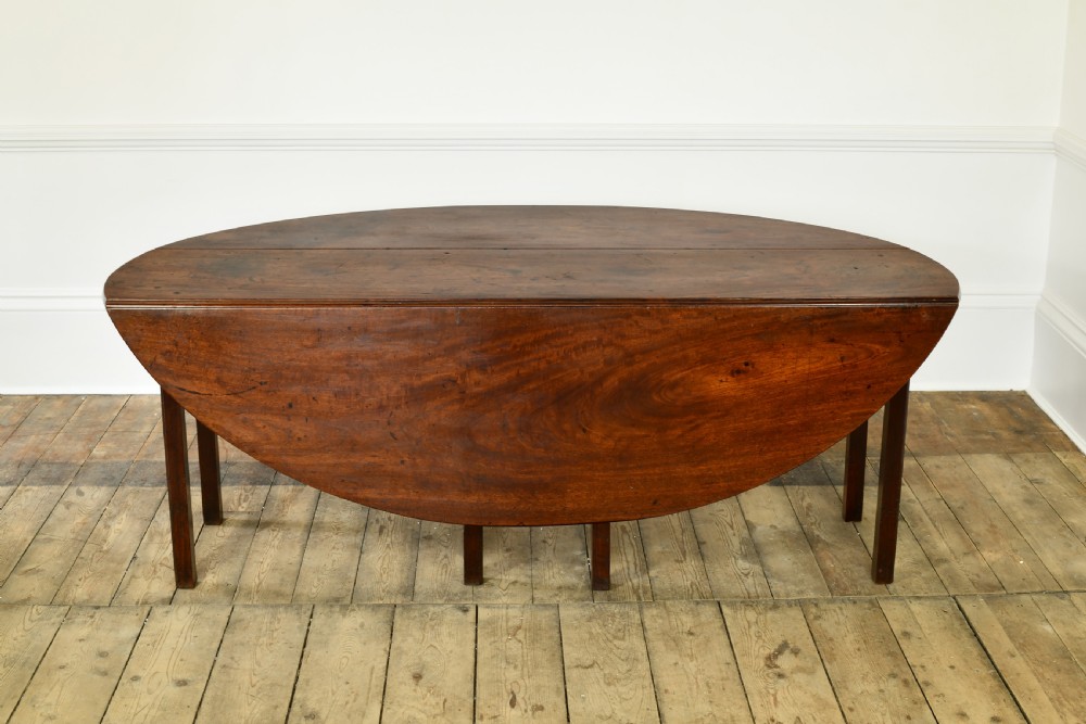 An 18th-century Irish mahogany hunt table featuring an oval drop-leaf top supported by straight wooden legs. View VI