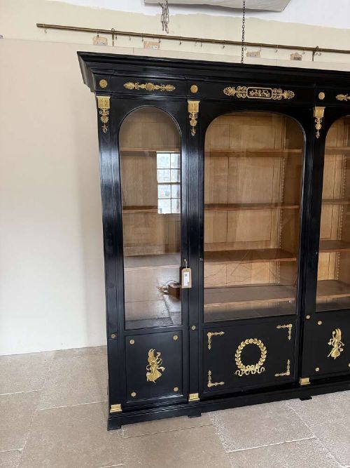 A large late 19th-century French Empire style ebonised bookcase with three arched glass doors, gilt bronze mounts, and light oak shelves. View II