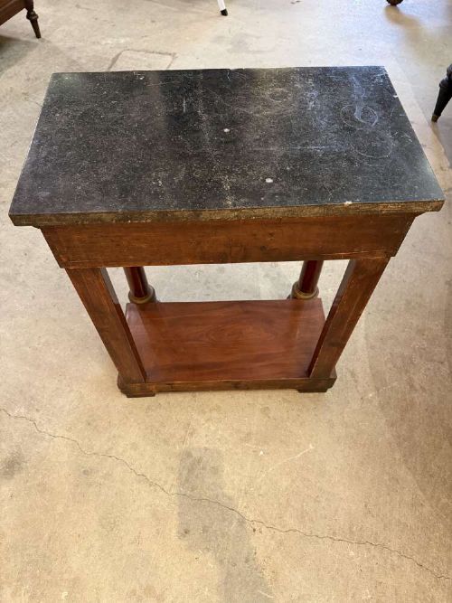 A small late nineteenth-century French Empire style mahogany console table featuring a black marble top, cylindrical column legs with metallic accents, a single frieze drawer with a brass laurel mount, and a lower shelf. View V