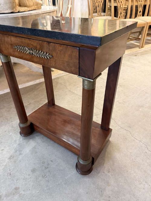 A small late nineteenth-century French Empire style mahogany console table featuring a black marble top, cylindrical column legs with metallic accents, a single frieze drawer with a brass laurel mount, and a lower shelf. View VII